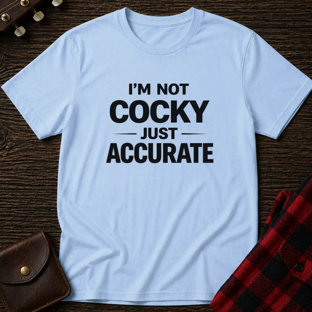 Light blue t-shirt with 'I'm not cocky just accurate' text on a wooden surface.